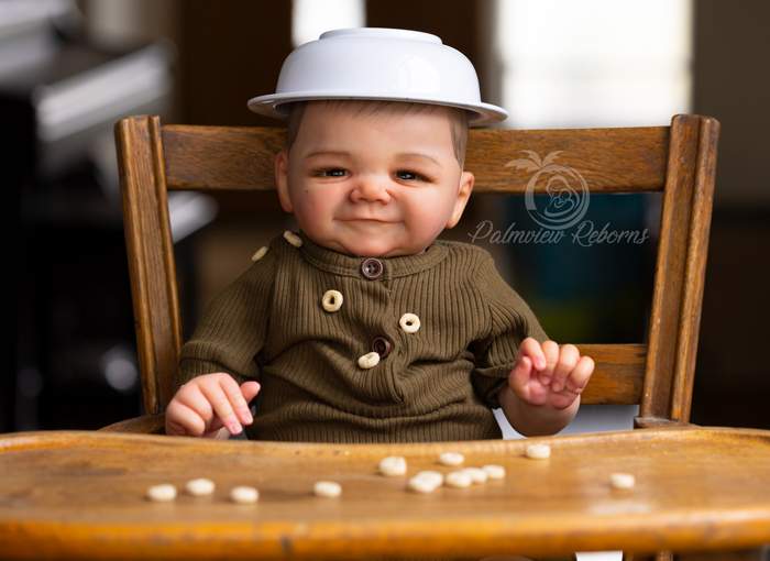 Reborn James by Sandy Faber in a highchair with a bowl on his head and cheerios spilled on his shirt